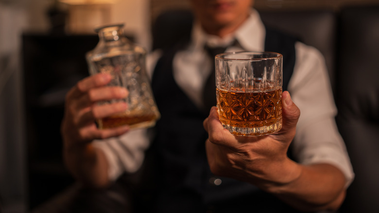 Bartender holding a bottle of bourbon and a glass of bourbon.